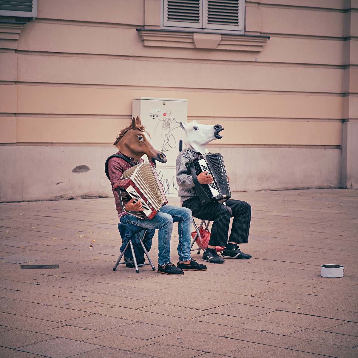 music two person wearing horse heads sitting on folding chairs while playing accordions beside brown concrete building accordion